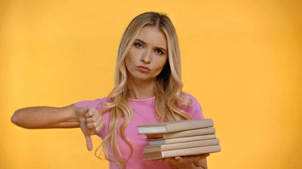 Скептична блондинка тримає книги і показує знак нелюбов ізольовано на жовтому — стокове фото