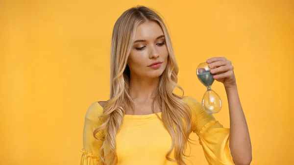 Donna bionda in camicetta che tiene la clessidra isolata sul giallo — Foto stock