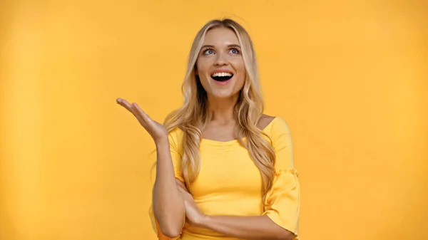 Mulher loira alegre apontando com a mão isolada no amarelo — Fotografia de Stock