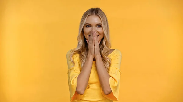 Glückliche Frau bedeckt Mund mit isolierten Händen auf gelb — Stockfoto
