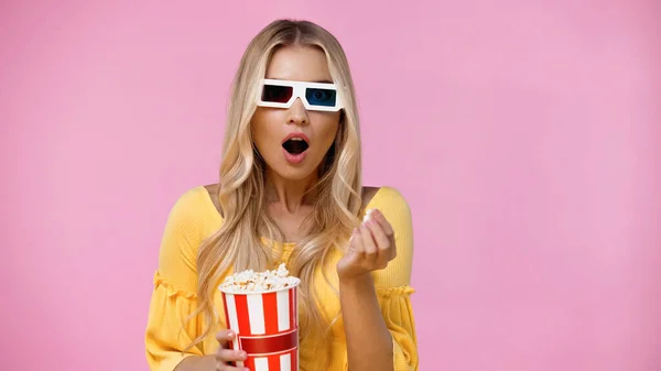 Schockierte blonde Frau in 3D-Gläsern hält Popcorn isoliert auf rosa — Stockfoto