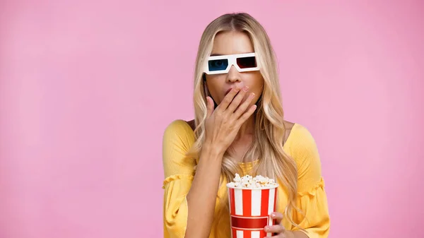 Schockierte Frau in 3D-Brille, die Mund bedeckt und Popcorn isoliert auf rosa hält — Stockfoto