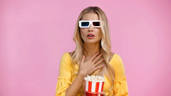 Беспокойная женщина в 3D очках держит ведро с попкорном, изолированным на розовый — стоковое фото