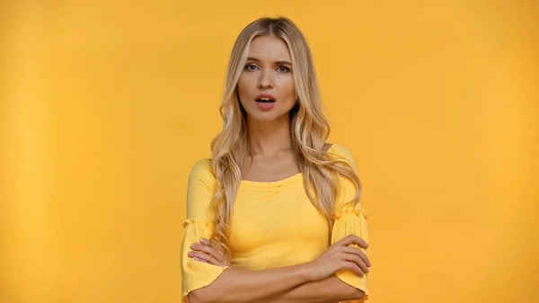 Embarrassed woman crossing arms and looking at camera isolated on yellow — Stock Photo