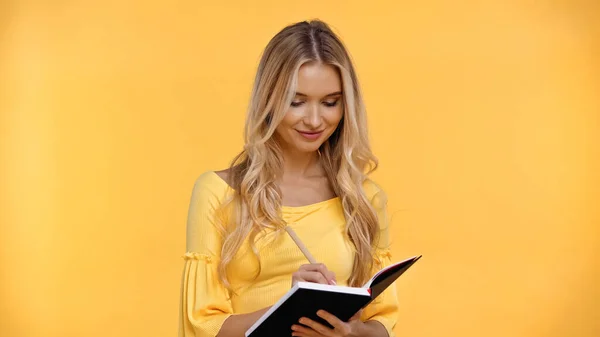 Sorrindo mulher loira escrevendo no caderno isolado no amarelo — Fotografia de Stock