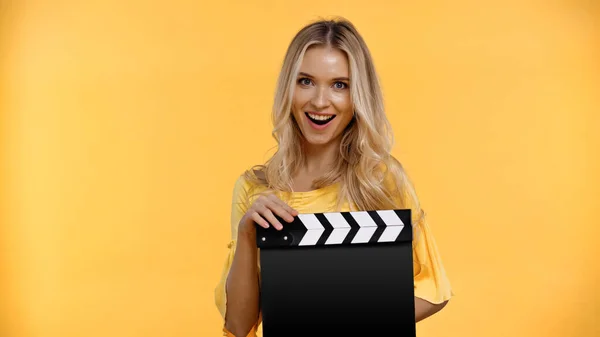 Cheerful blonde woman holding clapboard isolated on yellow — Stock Photo