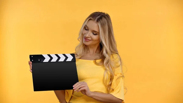 Smiling blonde woman in blouse holding clapboard isolated on yellow — Stock Photo
