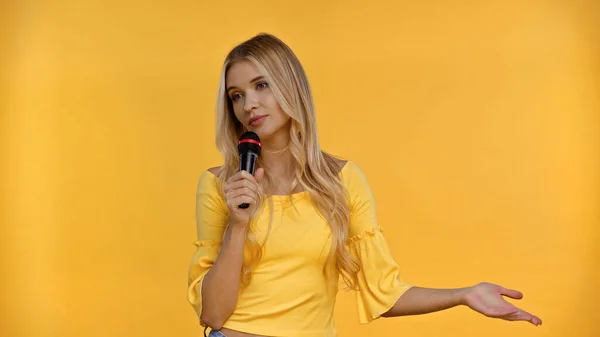 Mulher bonita na blusa segurando microfone isolado no amarelo — Fotografia de Stock