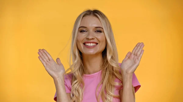 Heureuse femme blonde en t-shirt rose regardant la caméra isolée sur jaune — Photo de stock