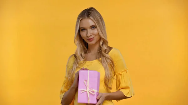 Весела блондинка тримає подарункову коробку ізольовано на жовтому — стокове фото