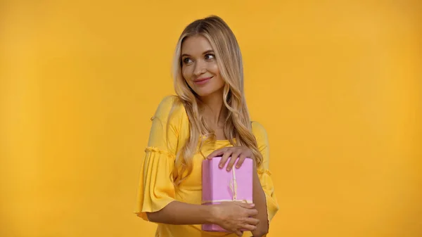 Smiling woman in blouse holding pink present isolated on yellow — Stock Photo