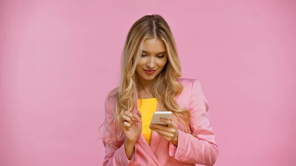 Hübsche blonde Frau in Jacke mit Handy isoliert auf rosa — Stockfoto