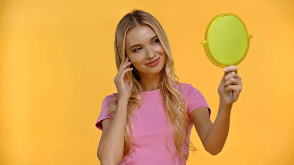 Smiling blonde woman holding mirror isolated on yellow — Stock Photo