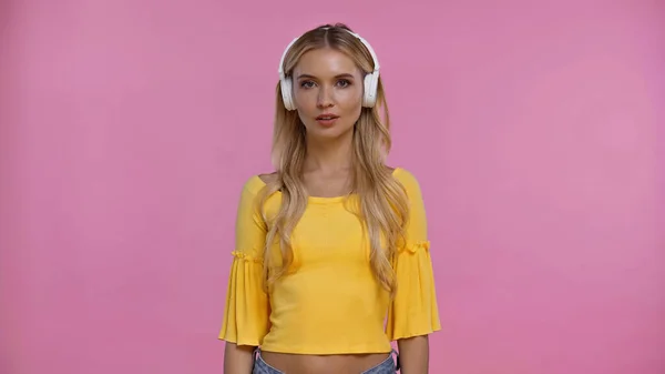 Mujer rubia en blusa y auriculares mirando a la cámara aislada en rosa - foto de stock