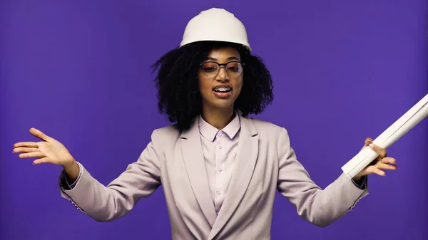 Smiling african american engineer with braces holding rolled paper isolated on purple — Stock Photo