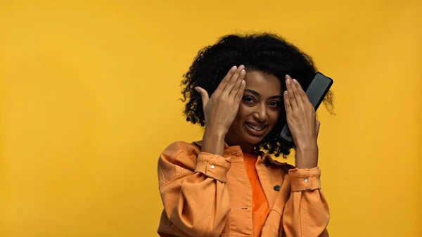 Femme afro-américaine gaie avec bretelles tenant télécommande isolé sur jaune — Photo de stock