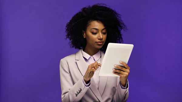 Young african american businesswoman in blazer holding digital tablet isolated on purple — Stock Photo