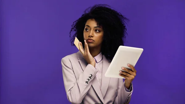 Jovem afro-americana em blazer segurando tablet digital e cartão de crédito isolado em roxo — Fotografia de Stock