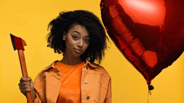 African american woman holding hammer near red heart-shaped balloon isolated on yellow, valentines day concept — Stock Photo