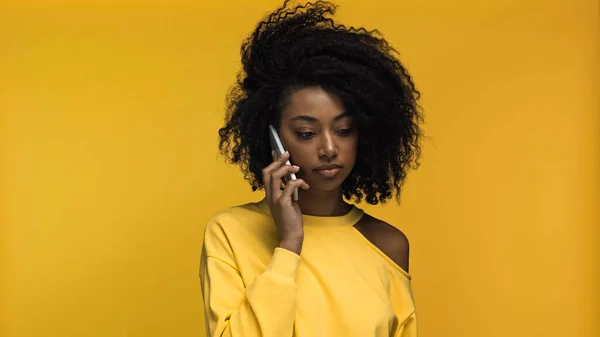 Joven afroamericana mujer hablando en celular aislado en amarillo - foto de stock