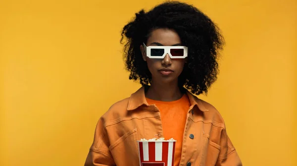 Jeune femme afro-américaine dans des lunettes 3d tenant seau de maïs soufflé isolé sur jaune — Photo de stock