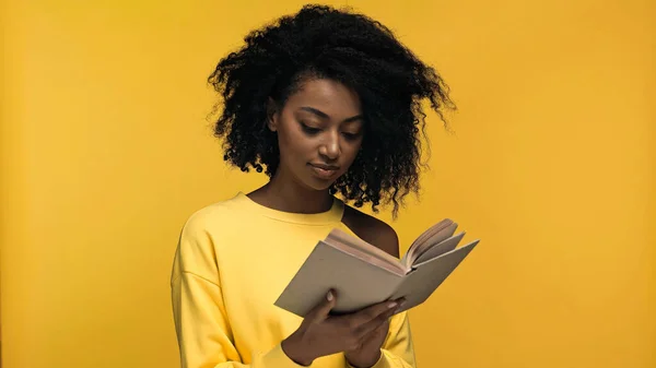 Encaracolado afro-americano mulher leitura livro isolado em amarelo — Fotografia de Stock