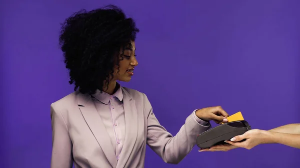 Усміхнена афроамериканська бізнес-леді в брекетах, що платять кредитною карткою ізольовано на фіолетовому — стокове фото