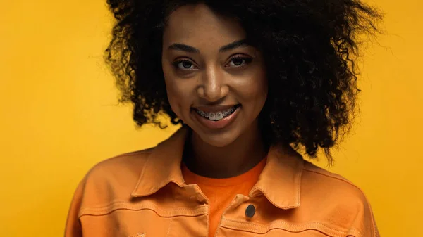 Позитивна афроамериканська жінка з брекетами посміхається ізольовано на жовтому — стокове фото