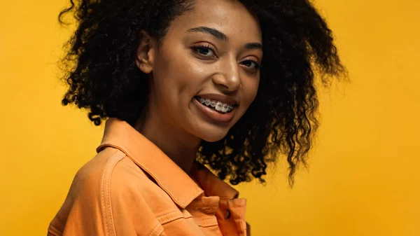 Gaie femme afro-américaine avec bretelles souriant isolé sur jaune — Photo de stock