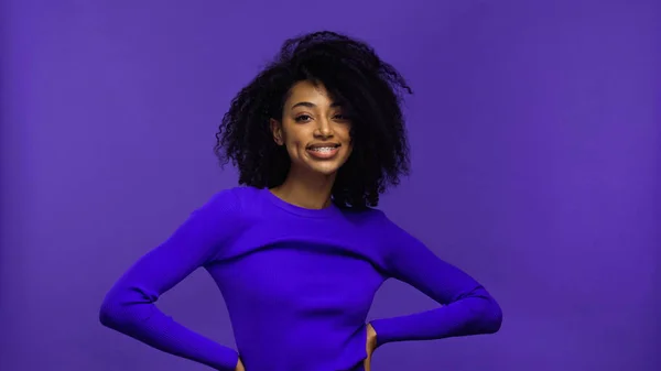 Cheerful african american young woman with braces looking at camera isolated on purple — Stock Photo