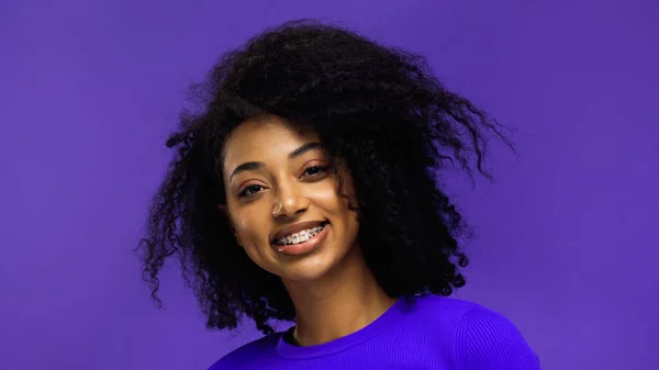 Радостная африканская американка с брекетами, улыбающимися изолированными на фиолетовый — стоковое фото