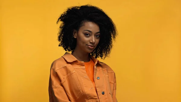Brünette afrikanisch-amerikanische Frau in orangefarbener Jacke isoliert auf gelb — Stockfoto