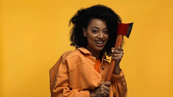 Brunette and cheerful african american woman with braces holding hammer isolated on yellow — Stock Photo