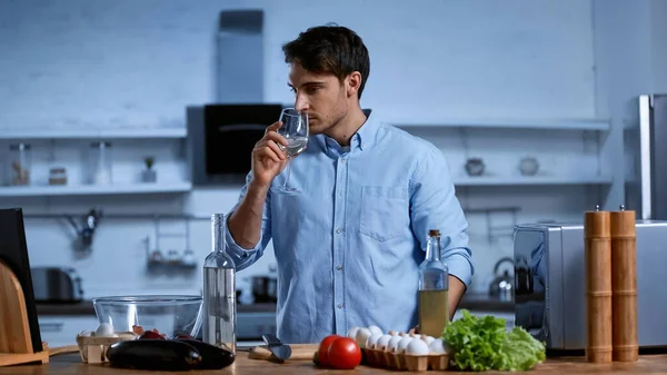 Giovane uomo che tiene il bicchiere e annusa vino bianco vicino alla tavola con ingredienti freschi — Foto stock