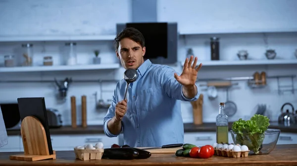 Homme excité chantant et tenant la poche de soupe près de la table avec des ingrédients frais — Photo de stock