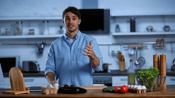 Giovane uomo gesticolare mentre in piedi vicino al tavolo con ingredienti freschi — Foto stock