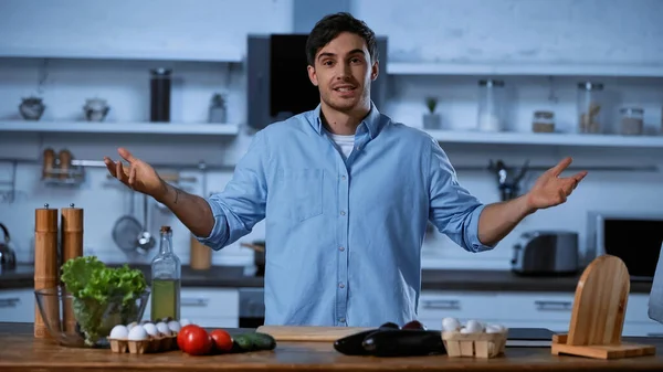 Young man looking at camera while gesturing near table with fresh ingredients — Stock Photo