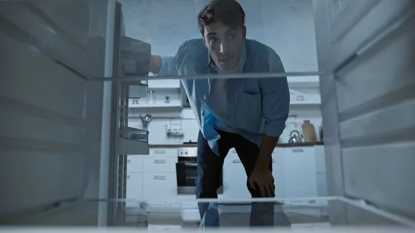 Curieux homme regardant dans le réfrigérateur vide dans la cuisine — Photo de stock