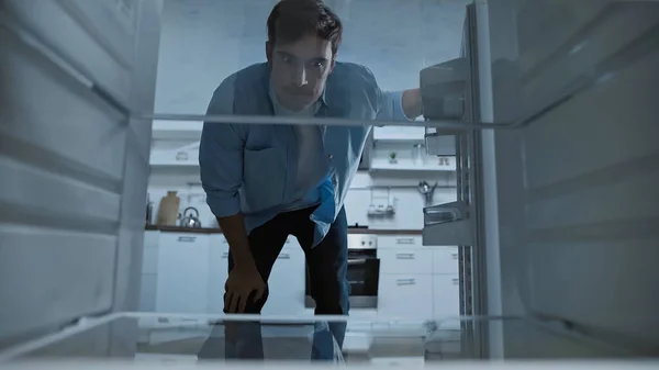 Незадоволений чоловік дивиться в порожній холодильник на кухні — стокове фото
