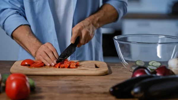 Vue recadrée de l'homme coupant des tomates près des aubergines floues et bol en verre — Photo de stock