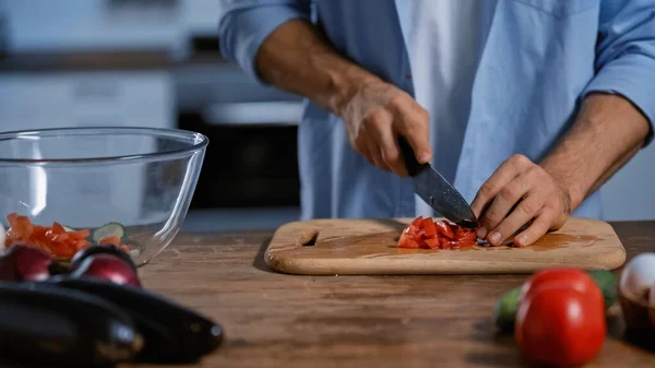 Vista recortada del hombre cortando tomates maduros cerca de berenjenas borrosas y cuenco de vidrio - foto de stock