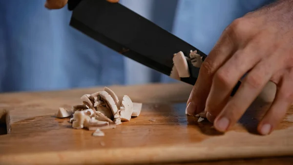 Vista recortada del hombre cortando setas en la tabla de cortar en la cocina - foto de stock