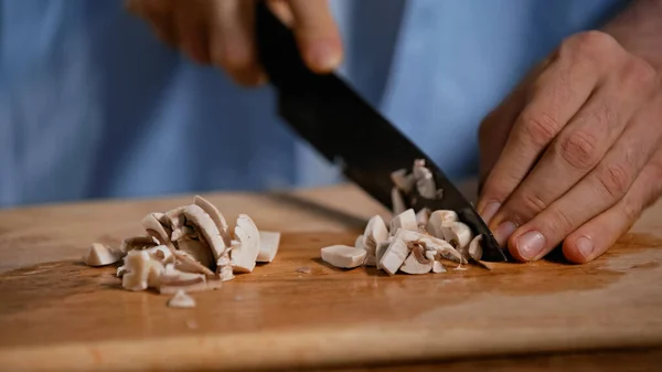 Cropped view of man cutting champignons on chopping board in kitchen — Stock Photo