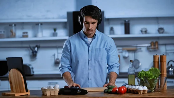 Joven con auriculares inalámbricos cocinando en la cocina - foto de stock