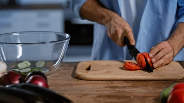 Abgeschnittene Ansicht eines Mannes, der Tomaten in der Nähe von verschwommenem Gemüse und Glasschale schneidet — Stockfoto