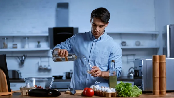 Jovem derramando vinho branco em vidro perto da mesa com legumes frescos — Fotografia de Stock