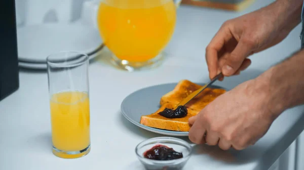 Partial view of man preparing toasts with confiture near orange juice — Stock Photo