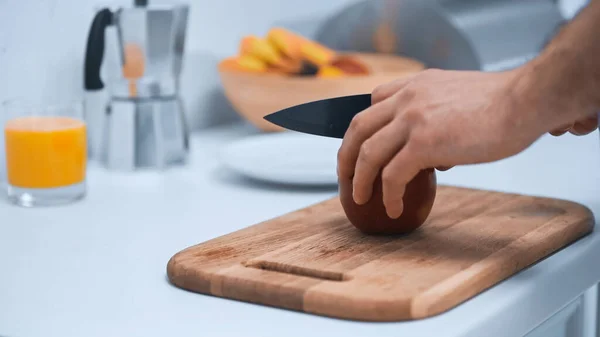 Vista parcial del hombre cortando manzana madura en la tabla de cortar en la cocina - foto de stock