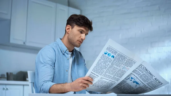 Чоловік у синій сорочці читає ранкову газету, сидячи на кухні — стокове фото