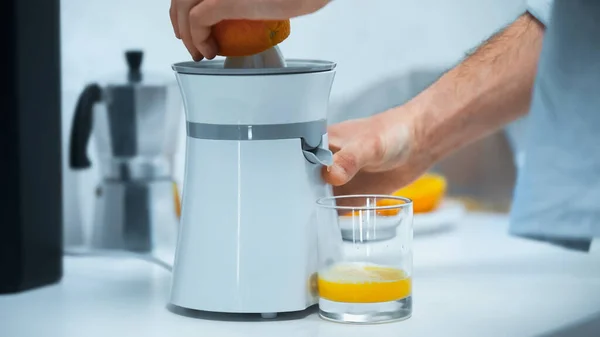 Cropped view of man preparing fresh orange juice on electric juicer in kitchen — Stock Photo
